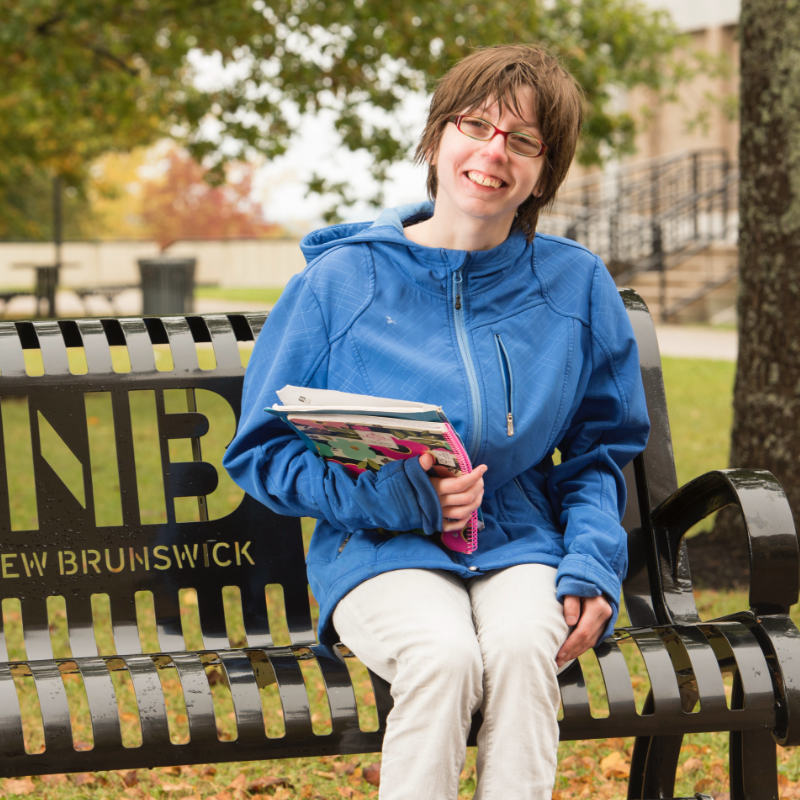 Personne assise sur un banc avec des livres à la main / Person sitting on a bench with books in hand