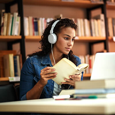 Youth wearing headphones sitting in front of a computer with an open book